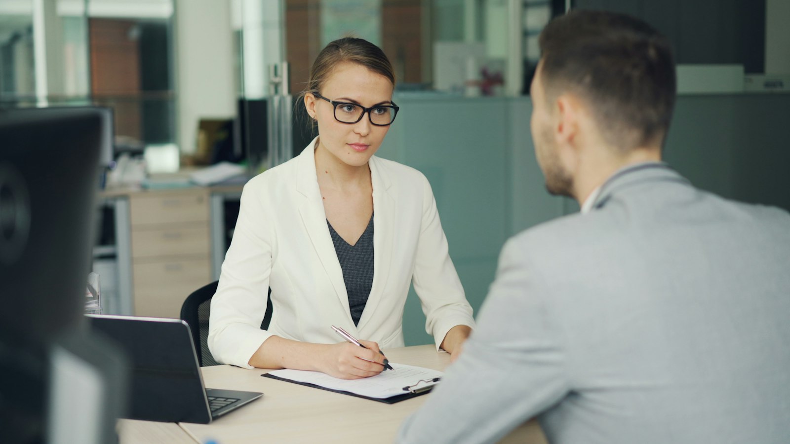 A recruiter in glasses interviewing a candidate across an office desk