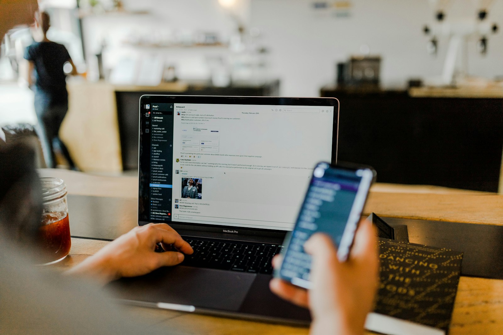 A person using a smartphone beside a laptop at a café table